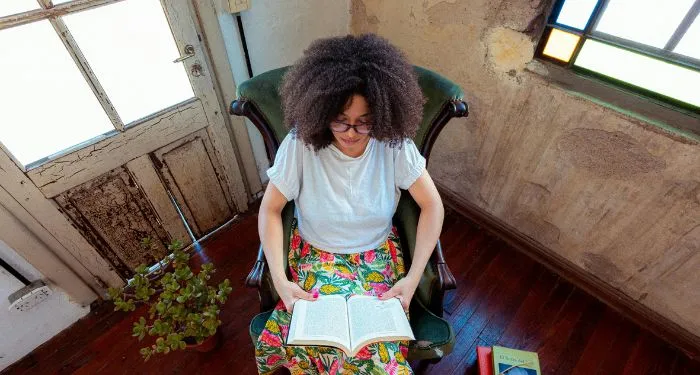light-skinned Black woman with big hair reading a book in a rustic house
